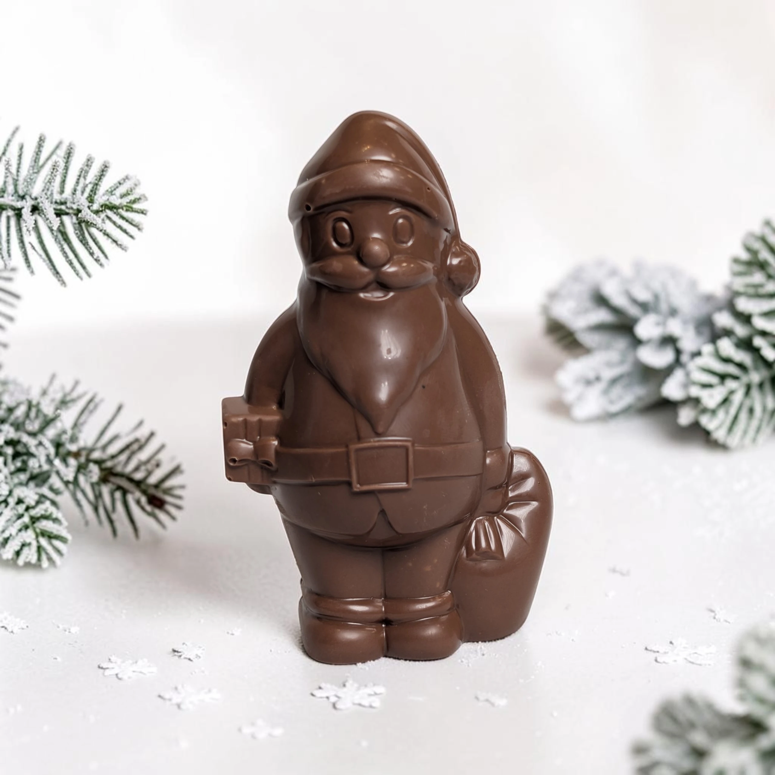 pere noel en chocolat au lait de la maison griess dans un décor de neige et branche de sapin